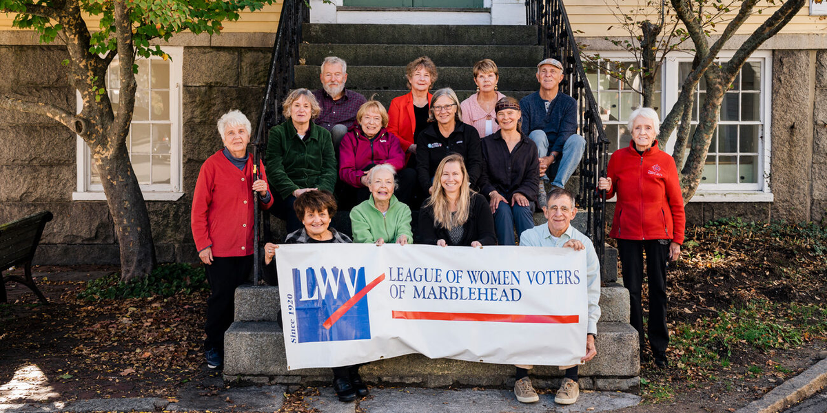 Adults posed on stone steps holding a League of Women Voters banner