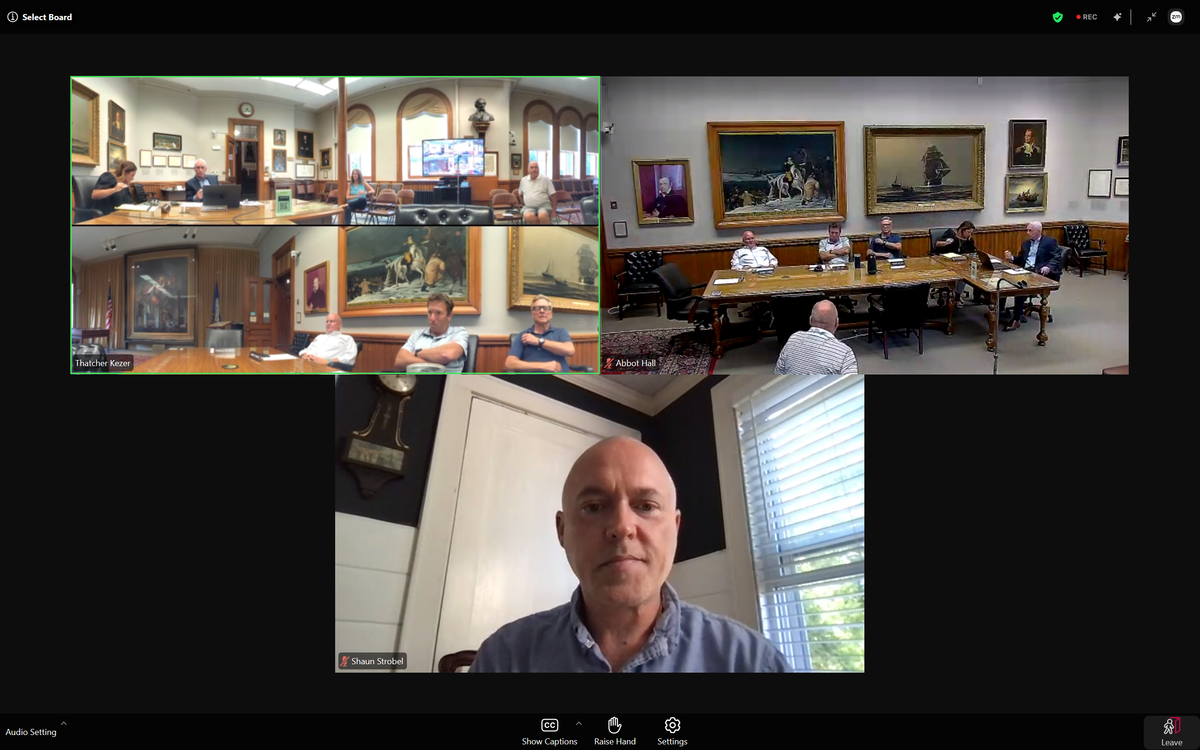 Videoconference grid showing a bald man on webcam and two paneled municipal meeting rooms